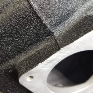 Close-up of black wrinkle powder coating on an automotive intake manifold showing dense, consistent texture